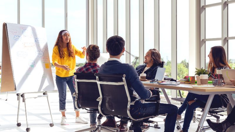 Personengruppe sitzend vor Frau an Flipchard