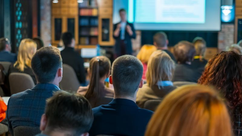 Rückansicht des Publikums, das den Rednern auf der Bühne zuhört