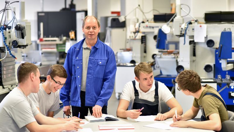 Vier sitzende Männer und ein Mann stehend