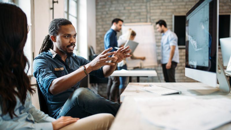 Frau und Mann sitzend im Gespräch mit zwei Personen im Hintergrund