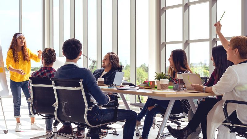 Personengruppe sitzend vor Frau an Flipchard