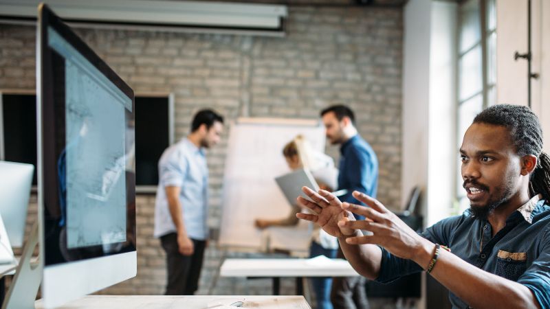 Mann vor Bildschirm mit zwei Personen im Hintergrund