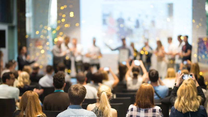 Sitzendes Publikum vor Personen auf einer Bühne mit goldenem Konfetti