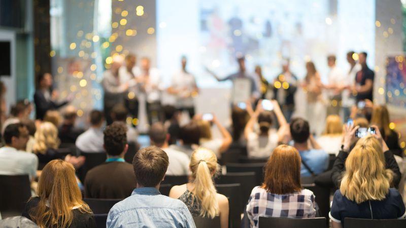 Sitzendes Publikum vor Personen auf einer Bühne mit goldenem Konfetti