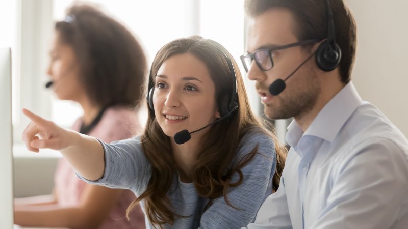 Frau und Mann mit Headsets vor Bildschirm