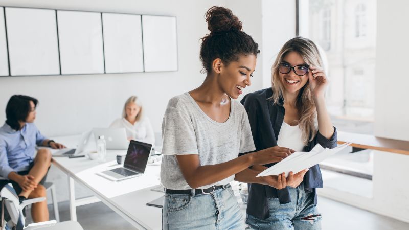 Zwei Frauen im Gespräch und im Hintergrund zwei Frauen an Tisch sitzend