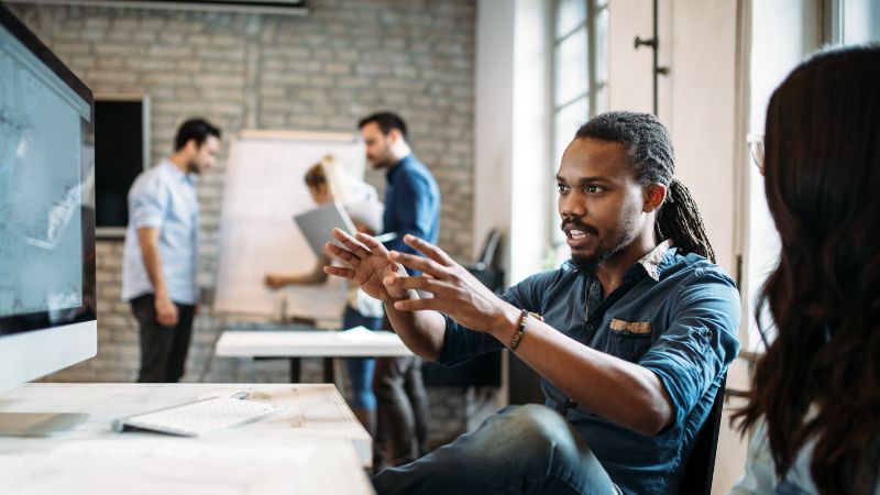 Frau und Mann sitzend im Gespräch und zwei Männer im Hintergrund